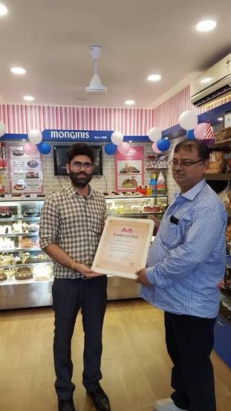 Two men holding a certificate inside a cake shop