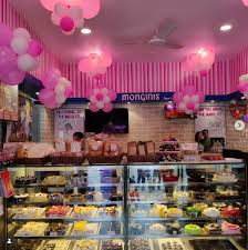 Cake shop decorated with pink balloons above a long display counter